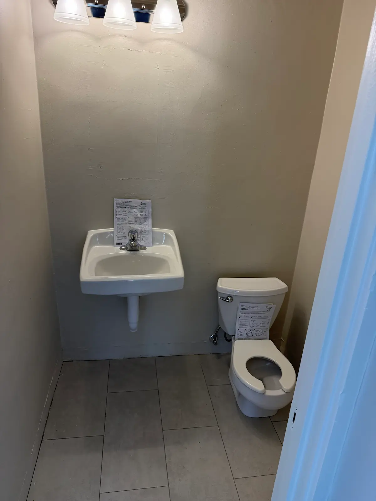 A newly completed commercial restroom showing a wall-mounted white porcelain sink and a standard white toilet installed on a gray tiled floor.