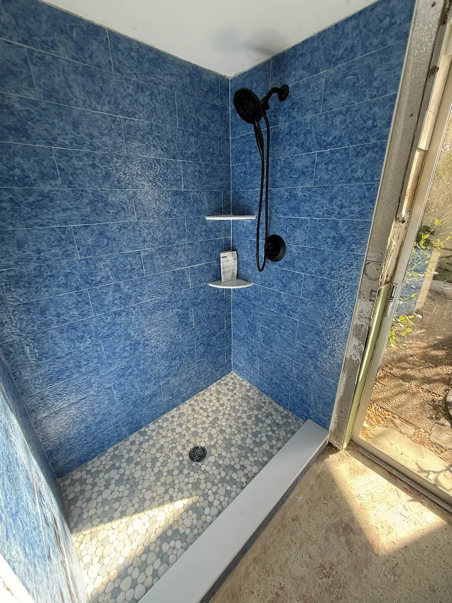 Elegant bathroom design showing a modern white soaking tub next to a glass-walled shower with beige stone tiling and a pebble mosaic floor insert.